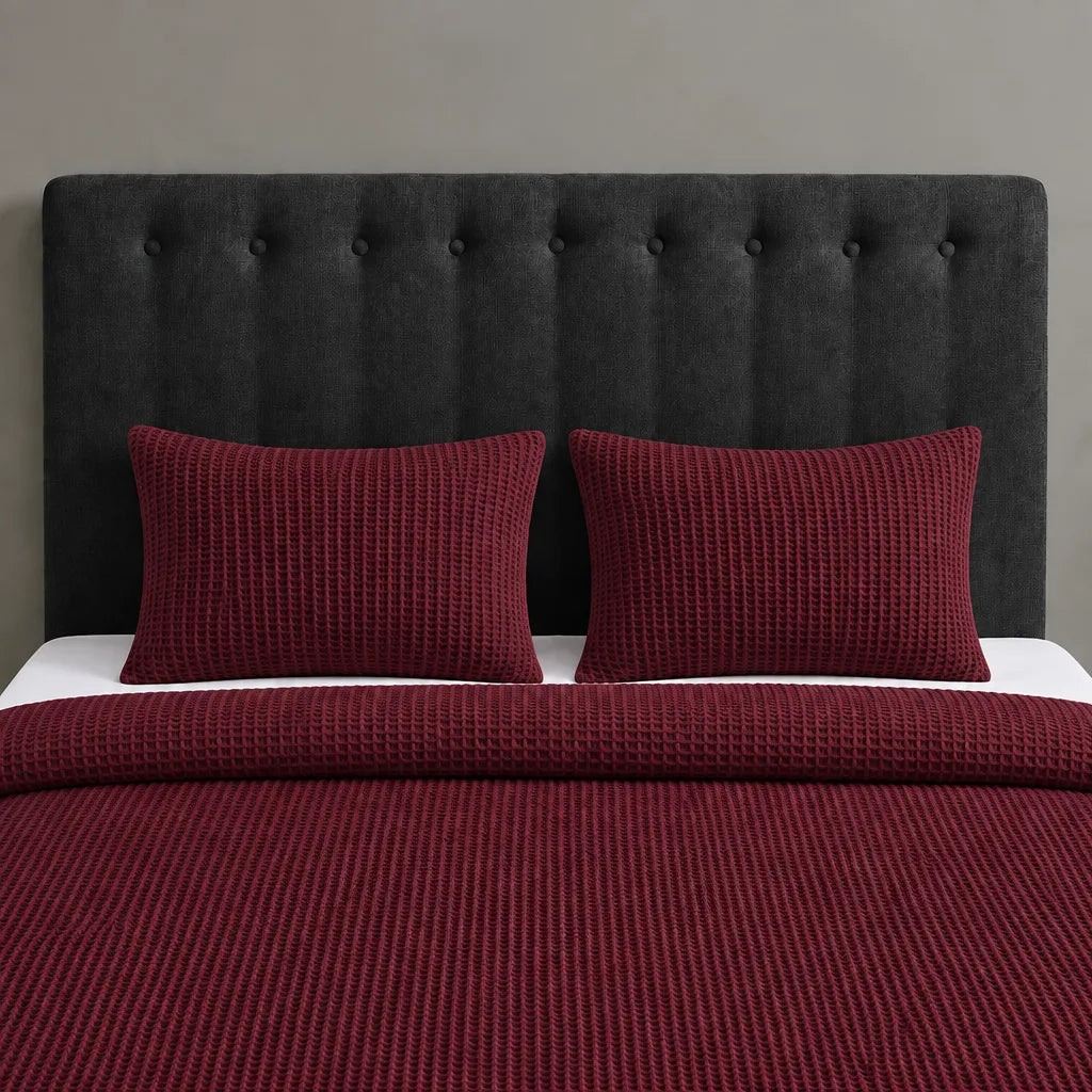 Burgundy textured blanket and two matching pillow covers on a bed with a black headboard