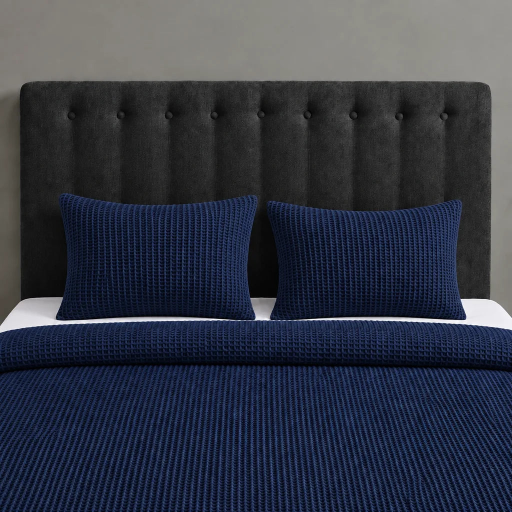 Navy blue textured blanket and two matching pillow covers on a bed with a black headboard