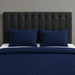 Navy blue textured blanket and two matching pillow covers on a bed with a black headboard