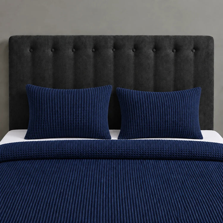 Navy blue textured blanket and two matching pillow covers on a bed with a black headboard