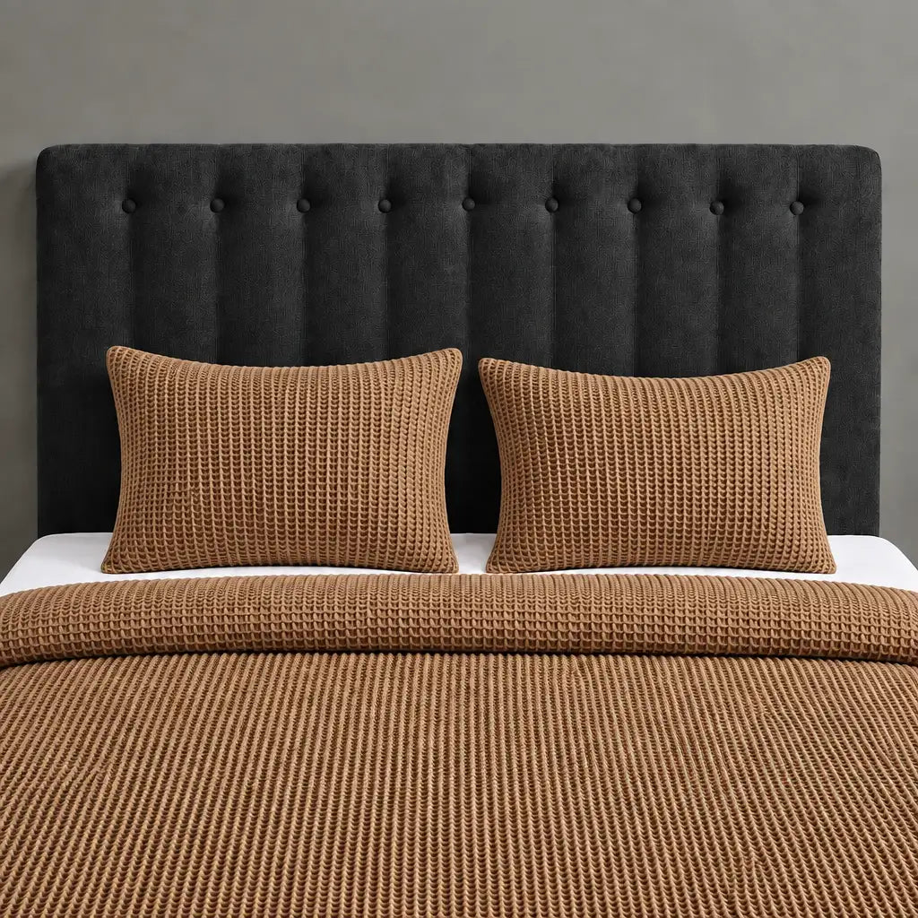 Brown textured blanket and two matching pillow covers on a bed with a black headboard