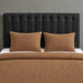 Brown textured blanket and two matching pillow covers on a bed with a black headboard