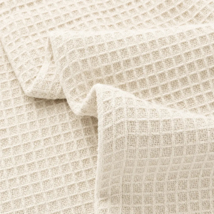 Close-up of a cream-colored waffle-weave fabric with a textured grid pattern, draped in soft folds.