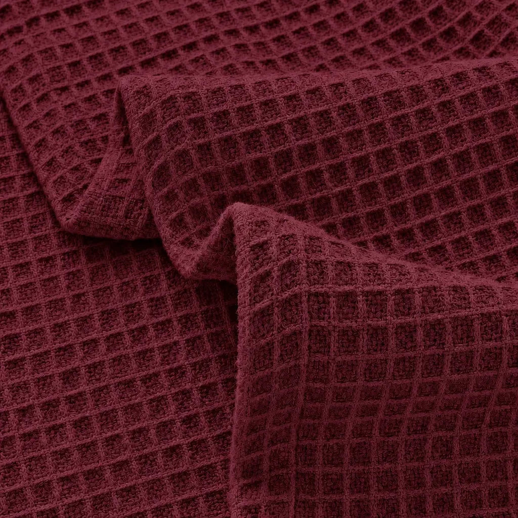 A close-up of a waffle-weave fabric in a deep burgundy or maroon color, draped to show its texture and pattern.
