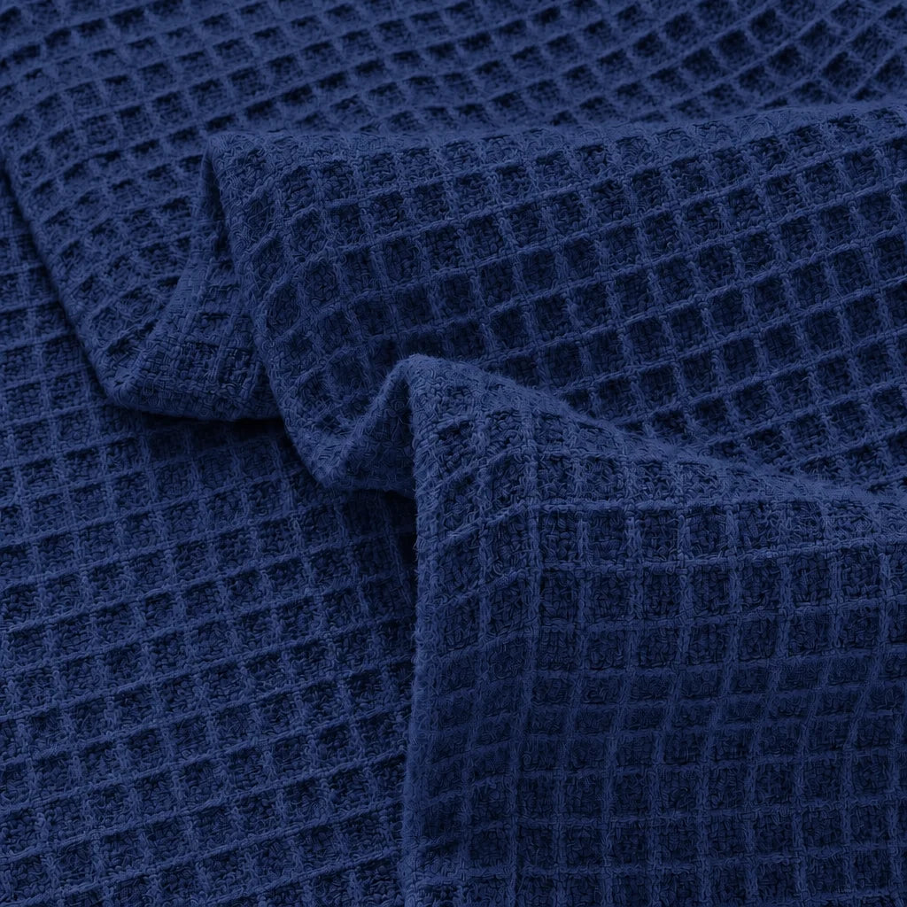 A close-up of dark navy blue waffle-weave fabric with a textured grid pattern, shown with soft folds.