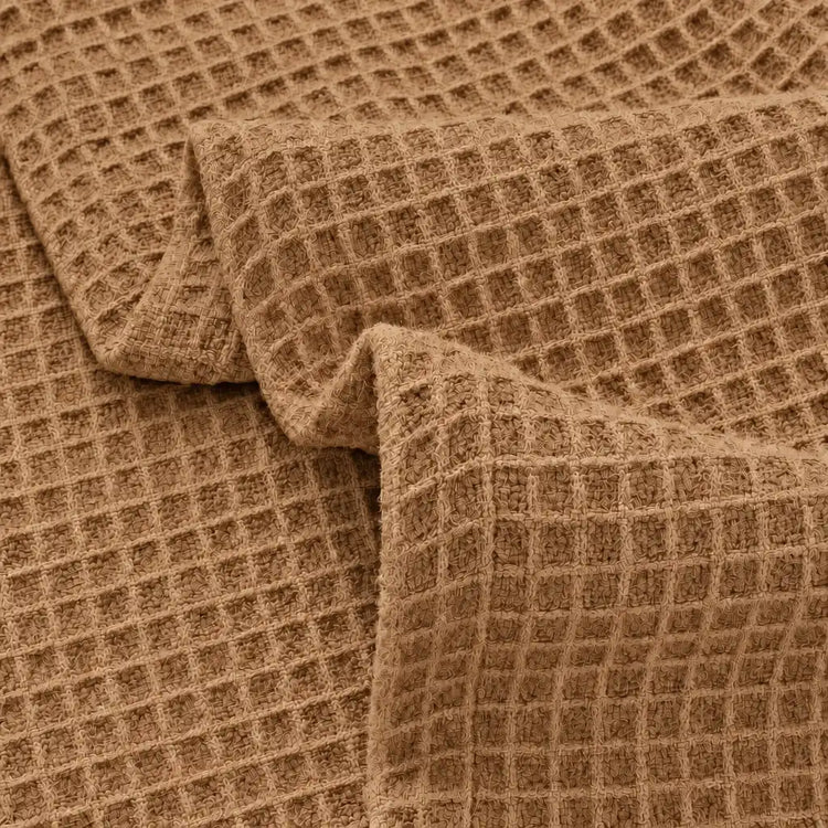 A close-up of a brown waffle-weave fabric with a textured grid pattern, shown draped in soft folds.