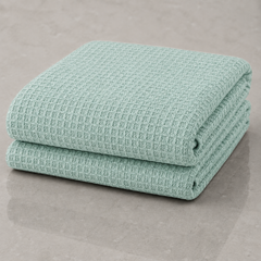 Two folded waffle-weave towels in a light mint green color, stacked on a neutral gray surface.
