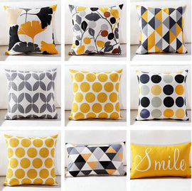 Yellow, grey, black and white cushion covers with leaves, dots, triangles and Smile lettering.