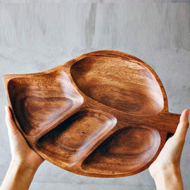Hands holding a brown leaf-shaped serving tray with four recessed compartments
