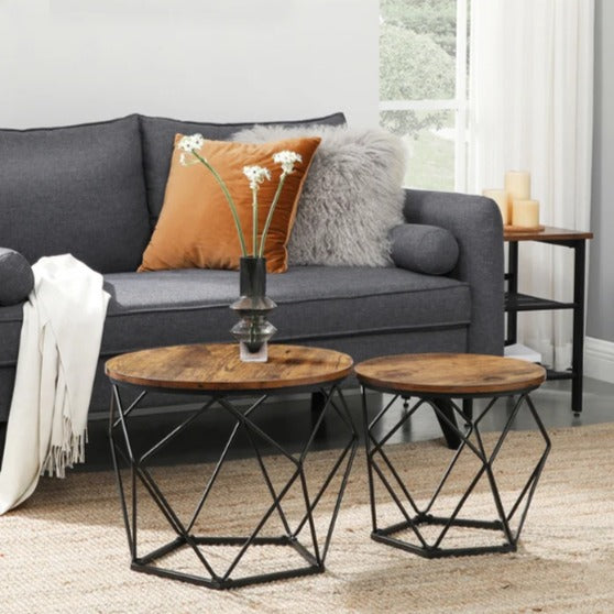 Two round brown nesting coffee tables with black geometric bases in front of a gray sofa.