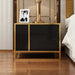 Black two-drawer bedside cabinet with gold-colored trim holding a lamp and framed photograph.