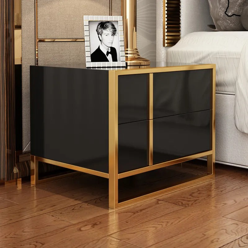 Angled view of a black bedside cabinet with gold-colored frame beside a bed.