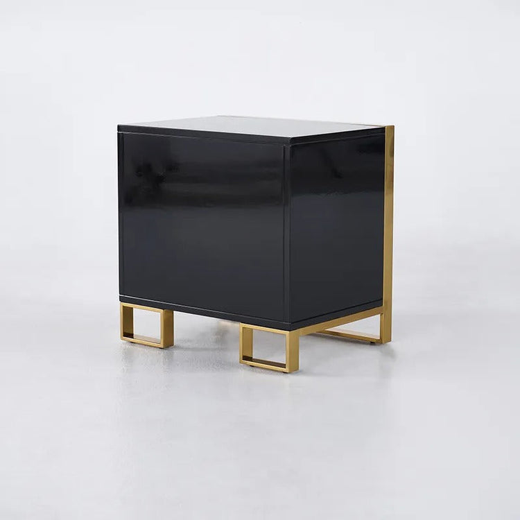 Rear angled view of a black bedside cabinet showing its plain back panel and gold-colored feet.