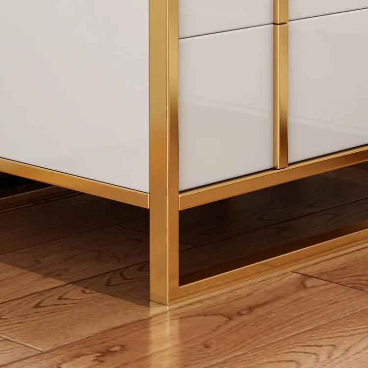Close-up of the white drawer fronts and gold-colored base frame of a bedside cabinet.