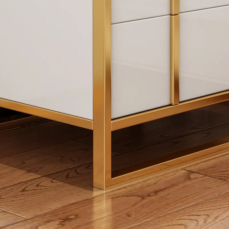 Close-up of the white drawer fronts and gold-colored base frame of a bedside cabinet.