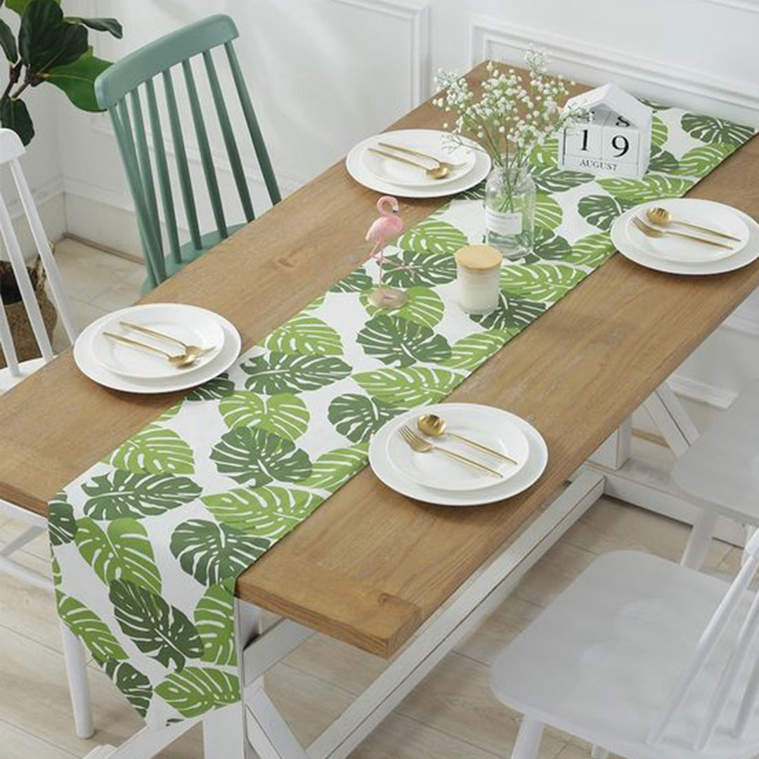 White table runner with large green tropical leaves on a dining table.