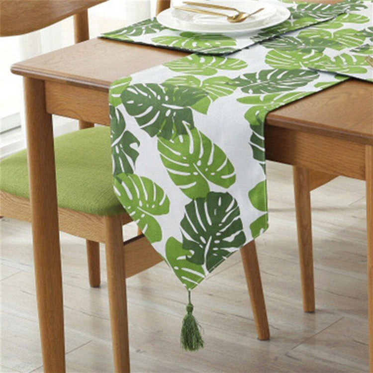 White table runner with large green tropical leaves on a dining table.
