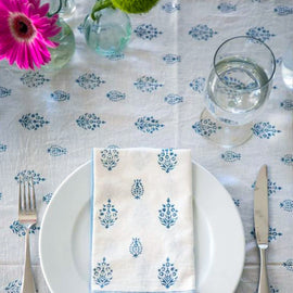 White tablecloth and napkin with small blue floral motifs beside a place setting.