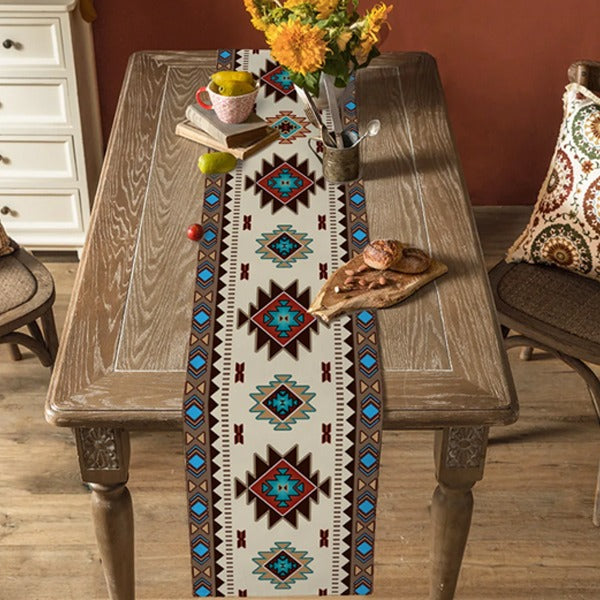 Cream table runner with red, turquoise and black geometric diamond motifs on a wooden table.