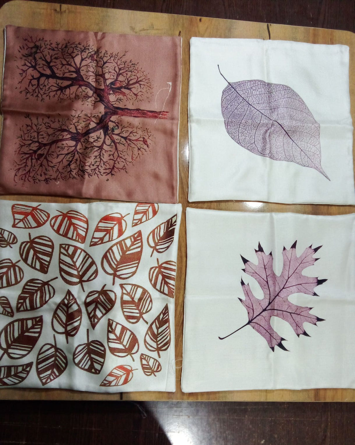 Four leaf print cushion covers laid flat on a wooden surface.