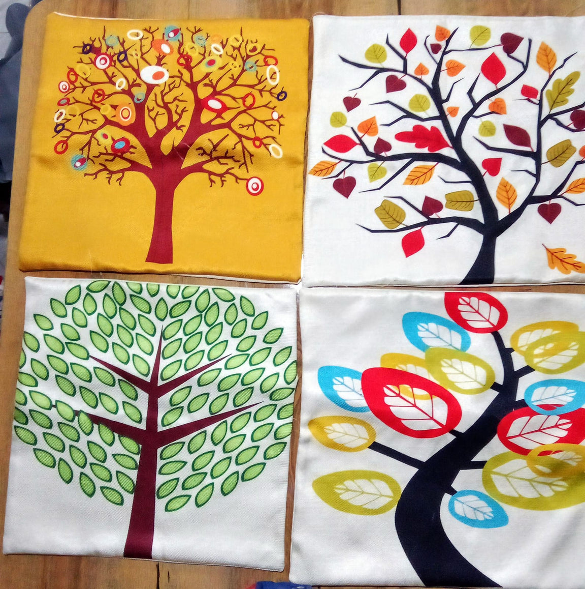 Four tree print cushion covers laid flat to show their colourful designs.