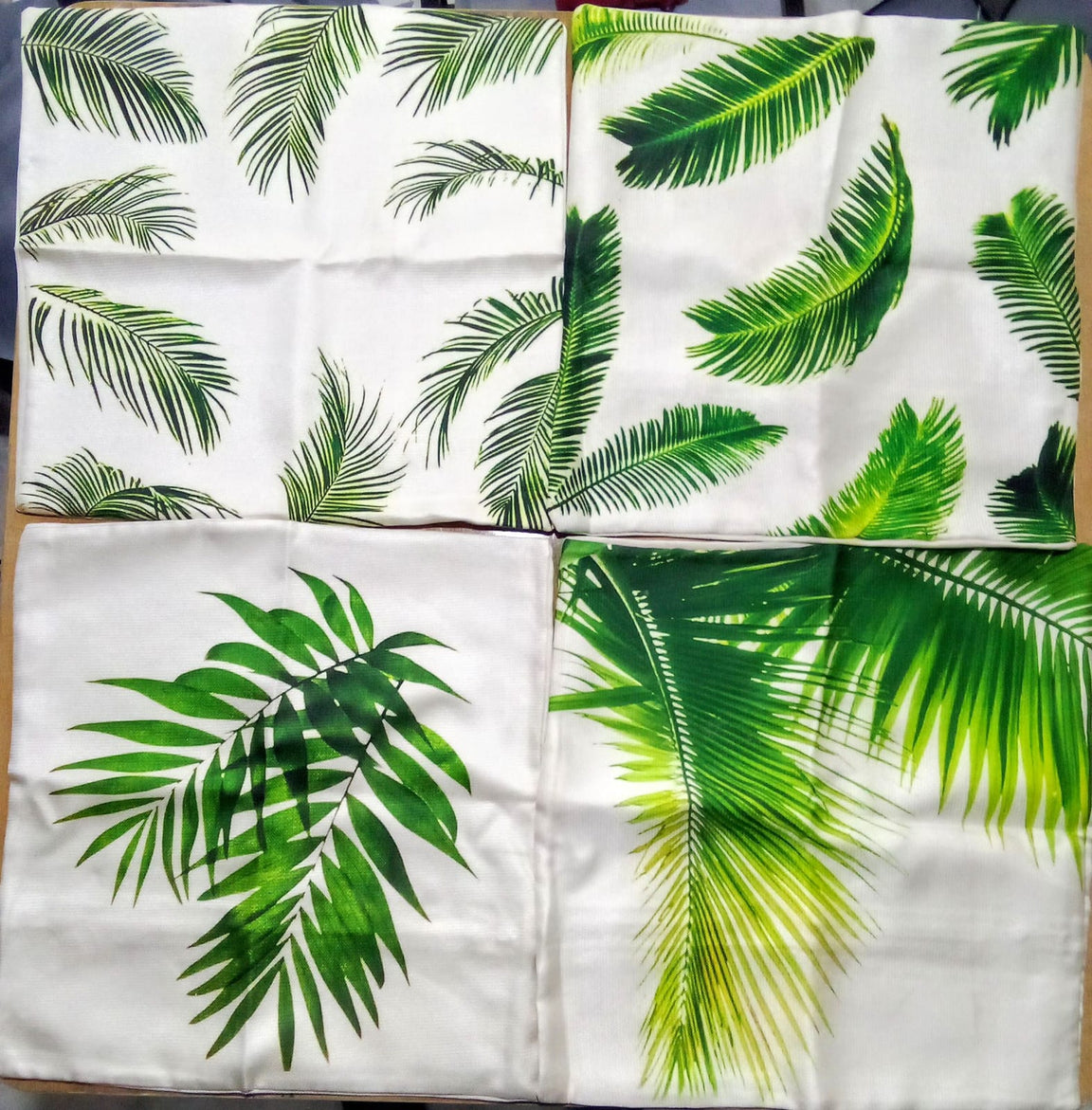 Four tropical leaf cushion covers laid flat to show the green leaf patterns.