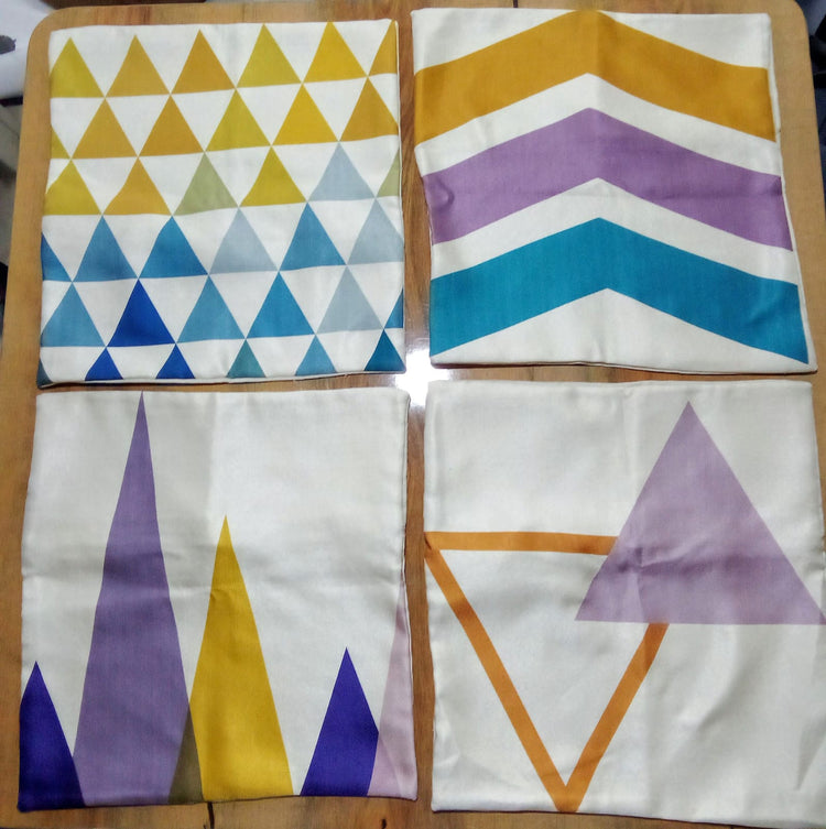 Four cushion covers laid flat with yellow, purple and blue geometric patterns.