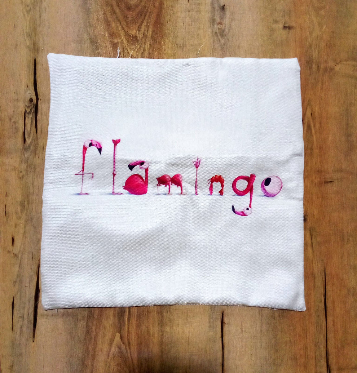 White cushion cover laid flat with pink Flamingo lettering.