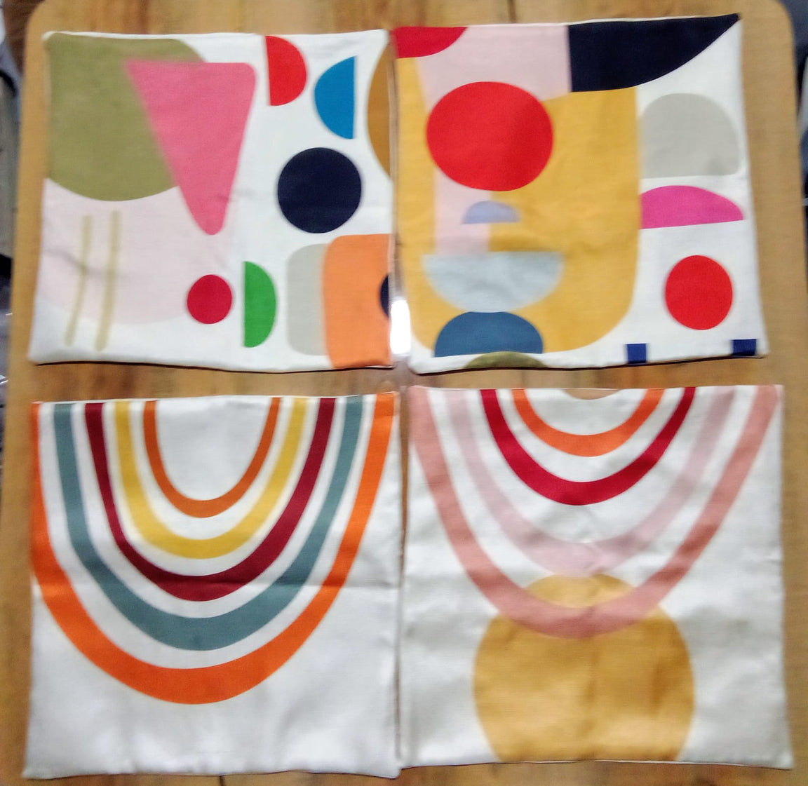 Abstract shape and rainbow cushion covers laid flat on a wooden surface.