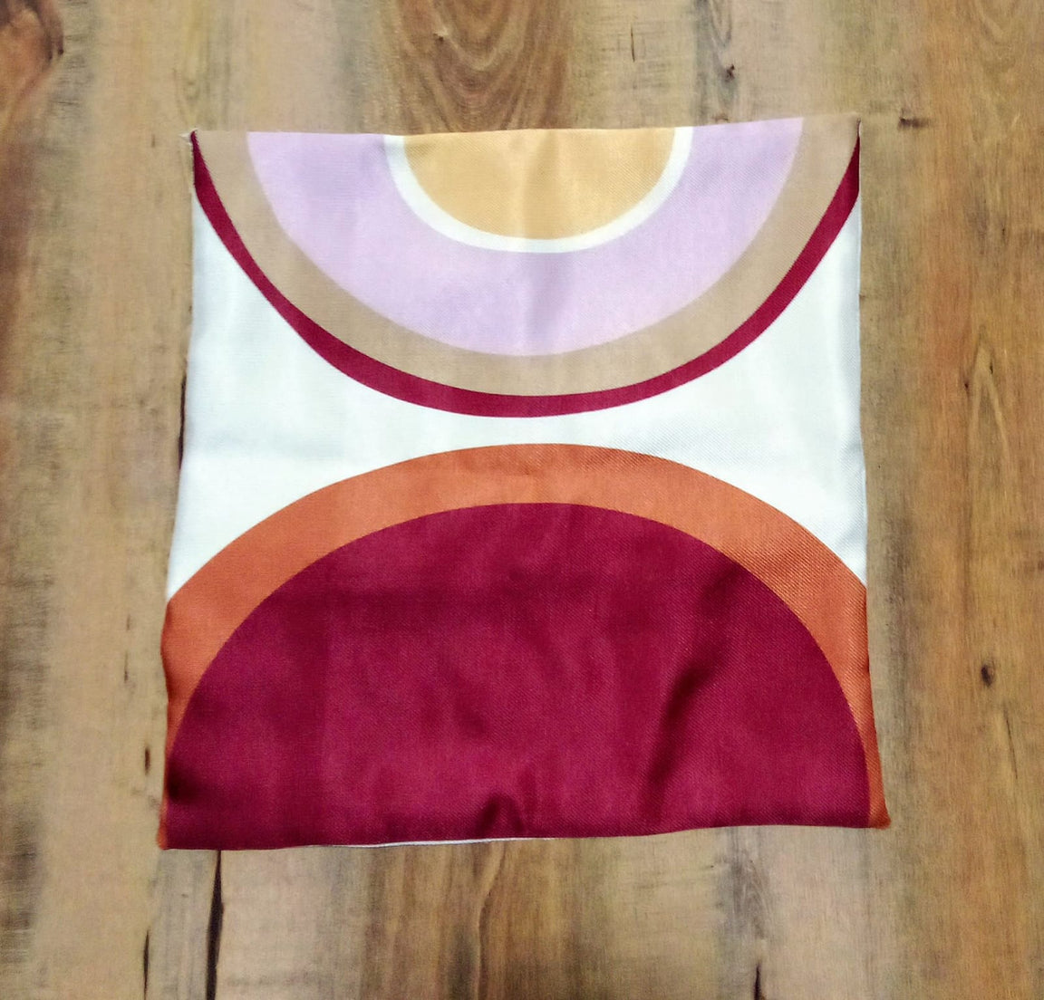 Cushion cover laid flat with large burgundy, orange and pale yellow semicircles.