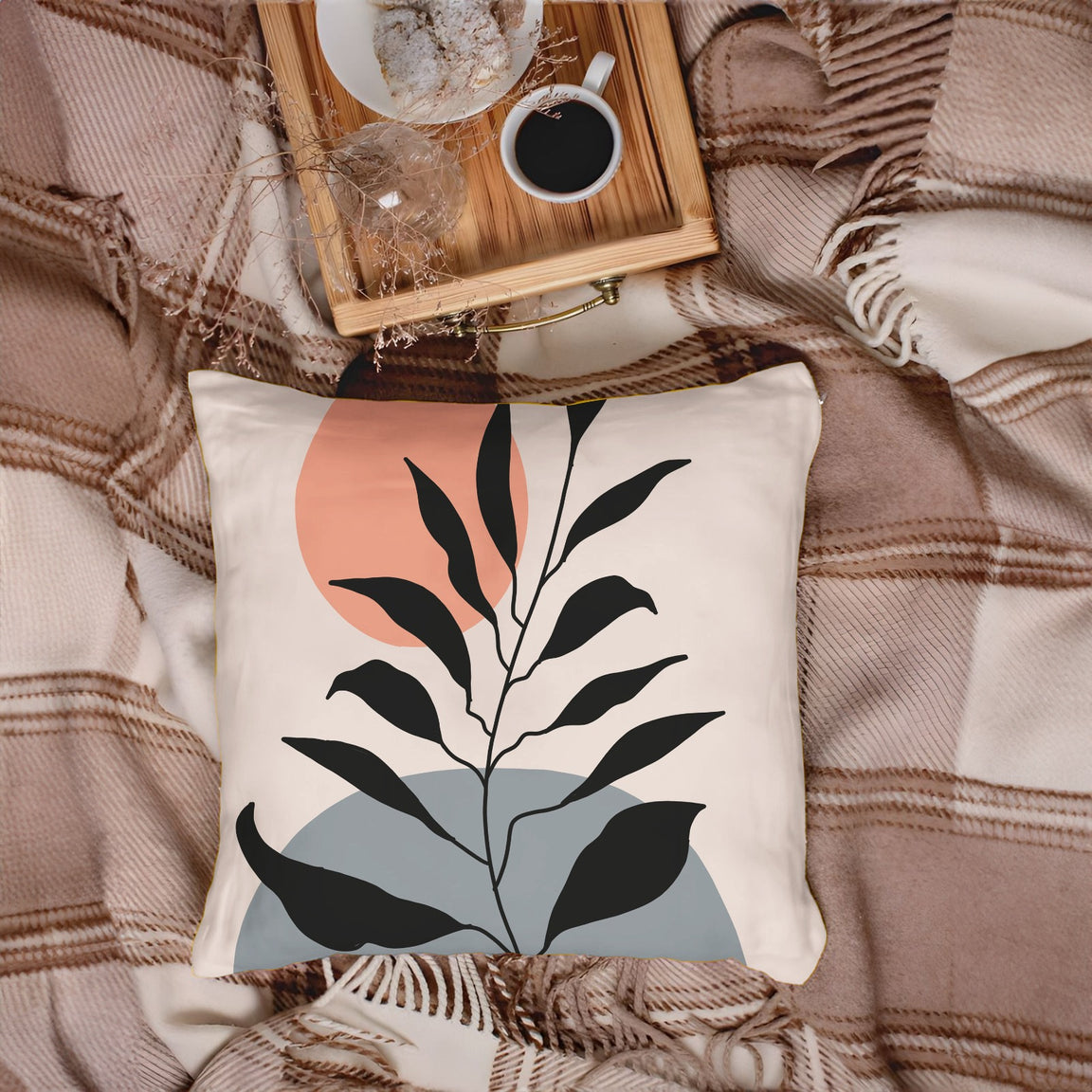Cream cushion cover with black leaves over grey and peach shapes.