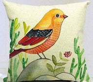 Cream cushion cover with a yellow and orange bird on a branch among green leaves.