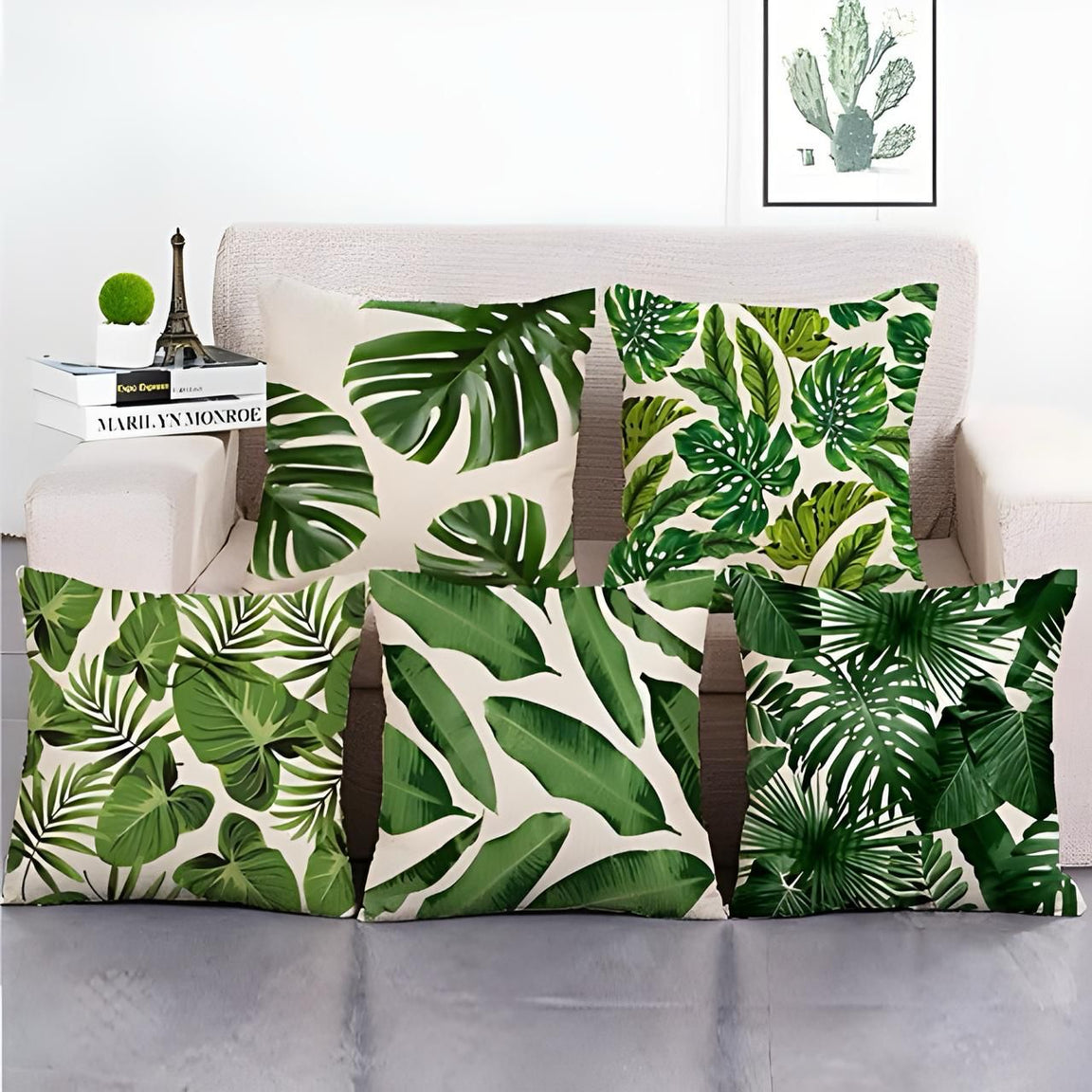 Five cream cushion covers with dense green tropical leaf prints displayed together.