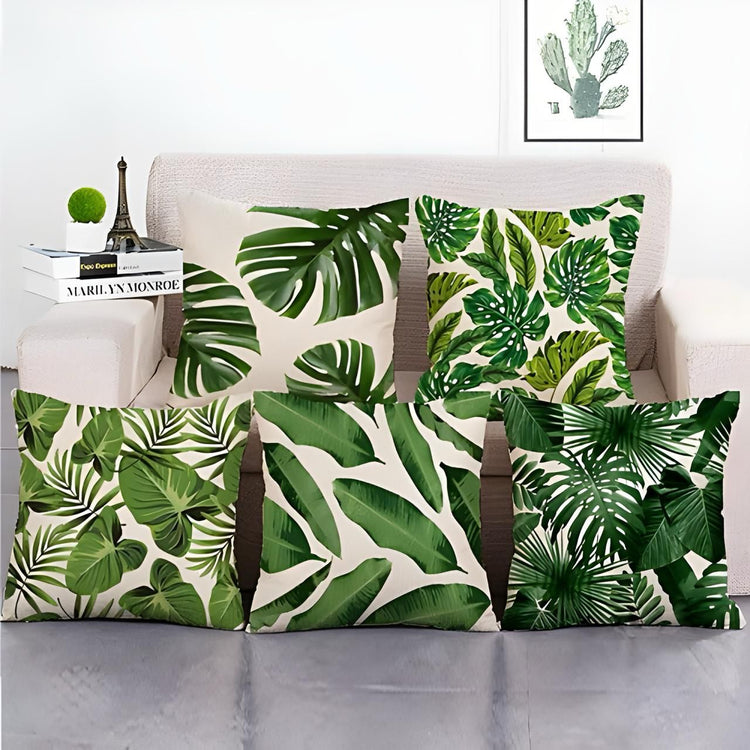 Five cream cushion covers with dense green tropical leaf prints displayed together.