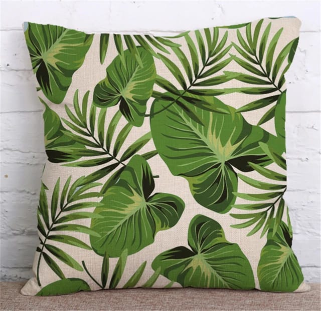 Cream cushion cover with overlapping green palm and broad tropical leaves.