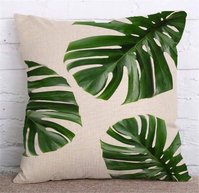 Cream cushion cover with three large green monstera leaves.