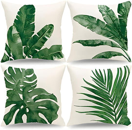 Four cream cushion covers with large green tropical leaf prints.