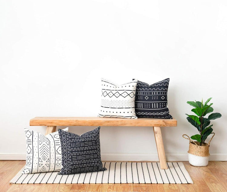 Black and white geometric cushion covers displayed on a wooden bench and the floor.