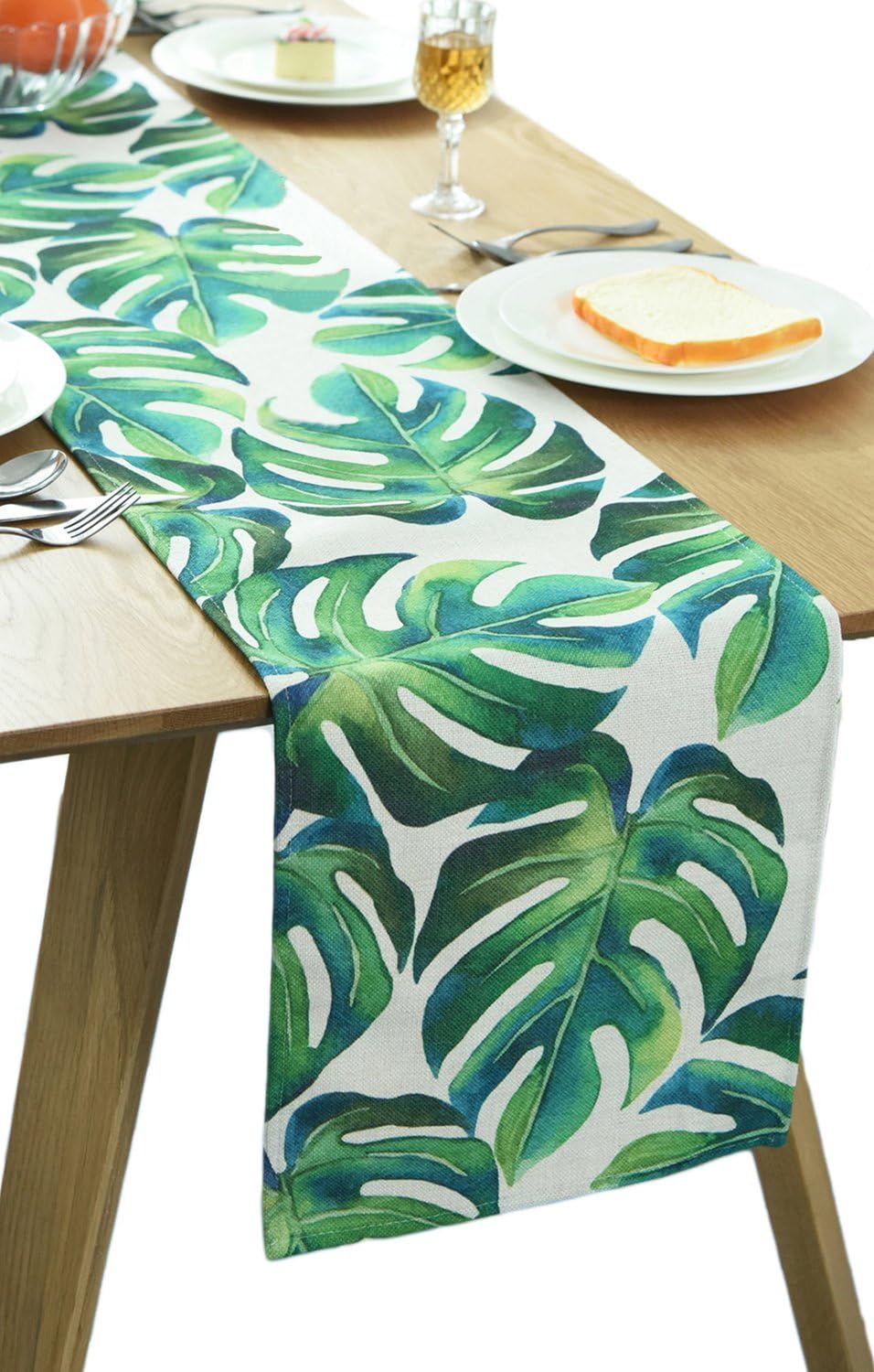 Green tropical-leaf table runner draped over the end of a dining table.