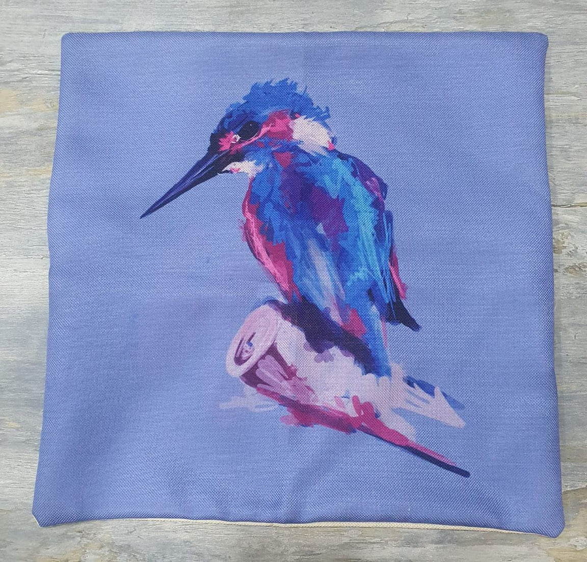 Blue cushion cover laid flat with a colourful kingfisher on a branch.