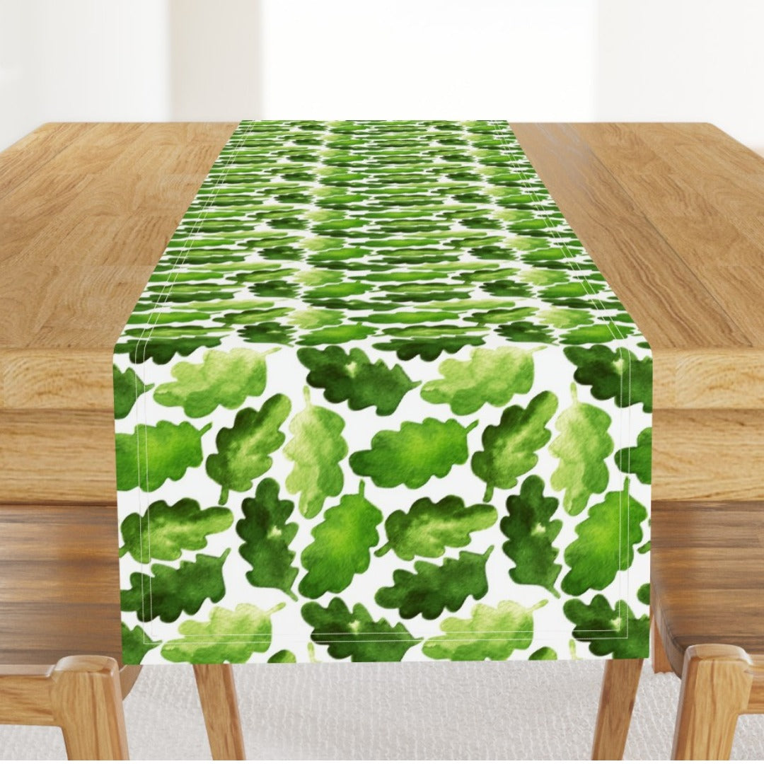 White table runner densely patterned with green leaves.