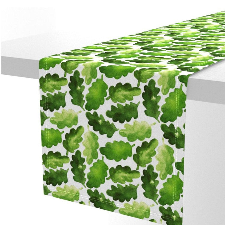White table runner densely patterned with green leaves.