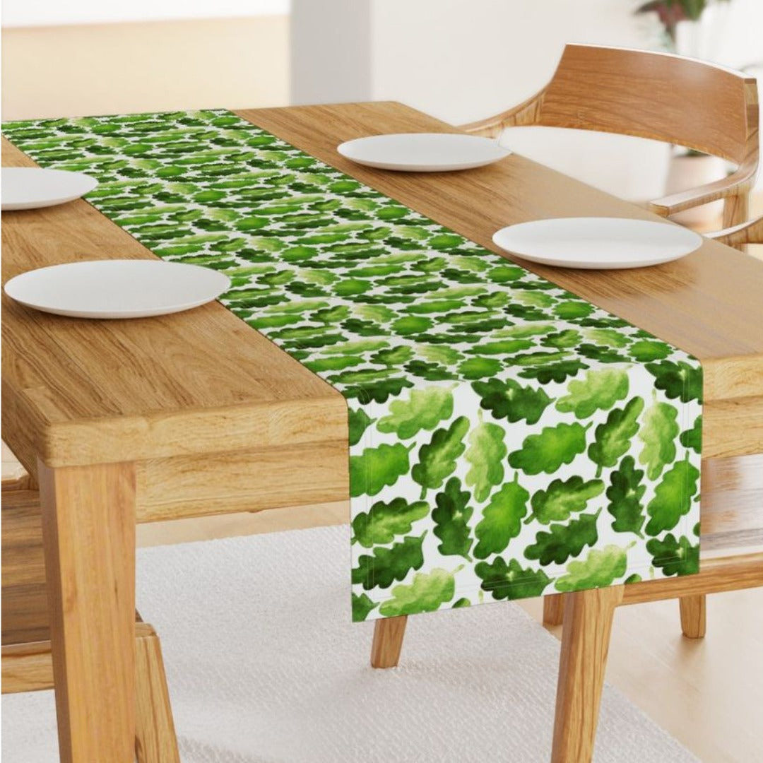 Green leafy-pattern table runner with a tasselled end on a wooden table.