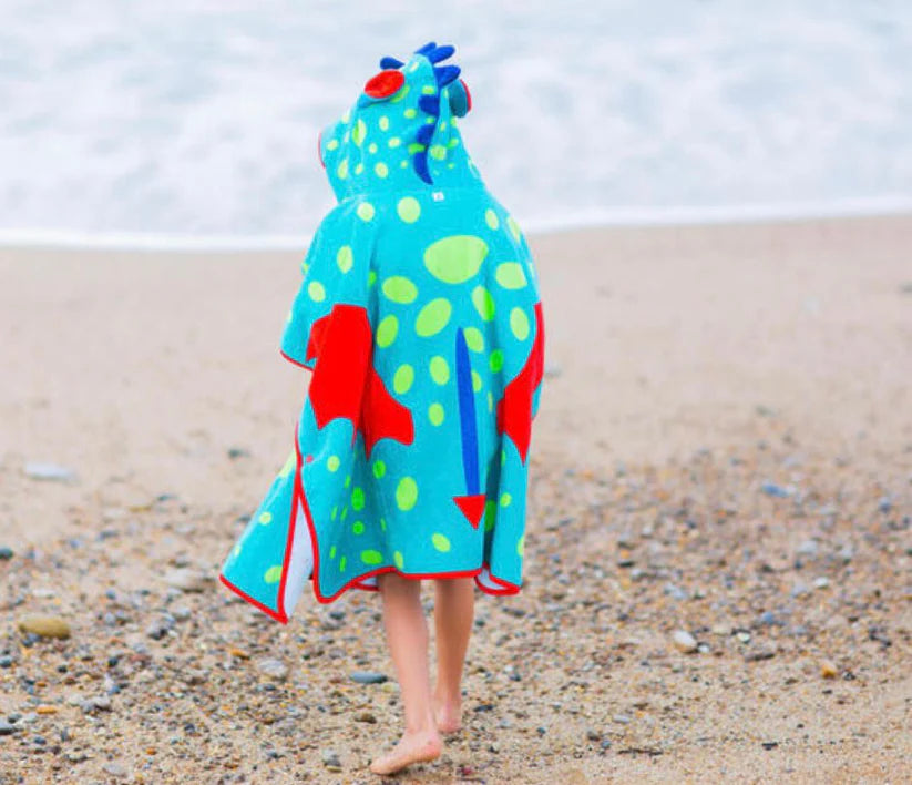 Back view of a child wearing a turquoise dinosaur towel poncho on a beach.