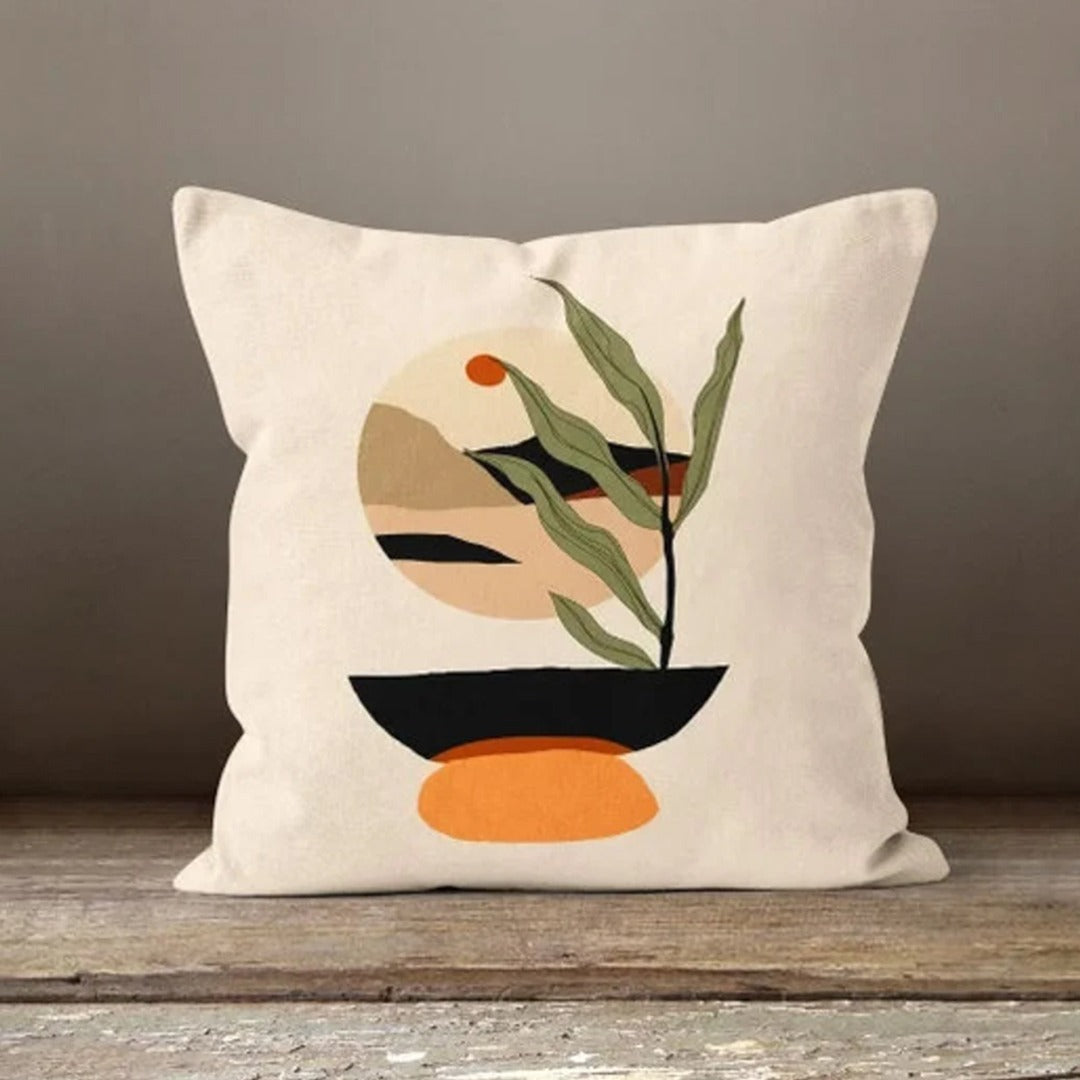 Cream cushion cover with a green leafy stem over orange, beige and black abstract shapes.