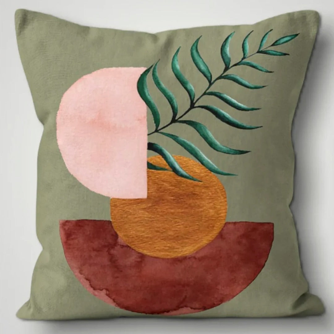 Sage green cushion cover with a teal leafy sprig over pink, ochre and rust shapes.