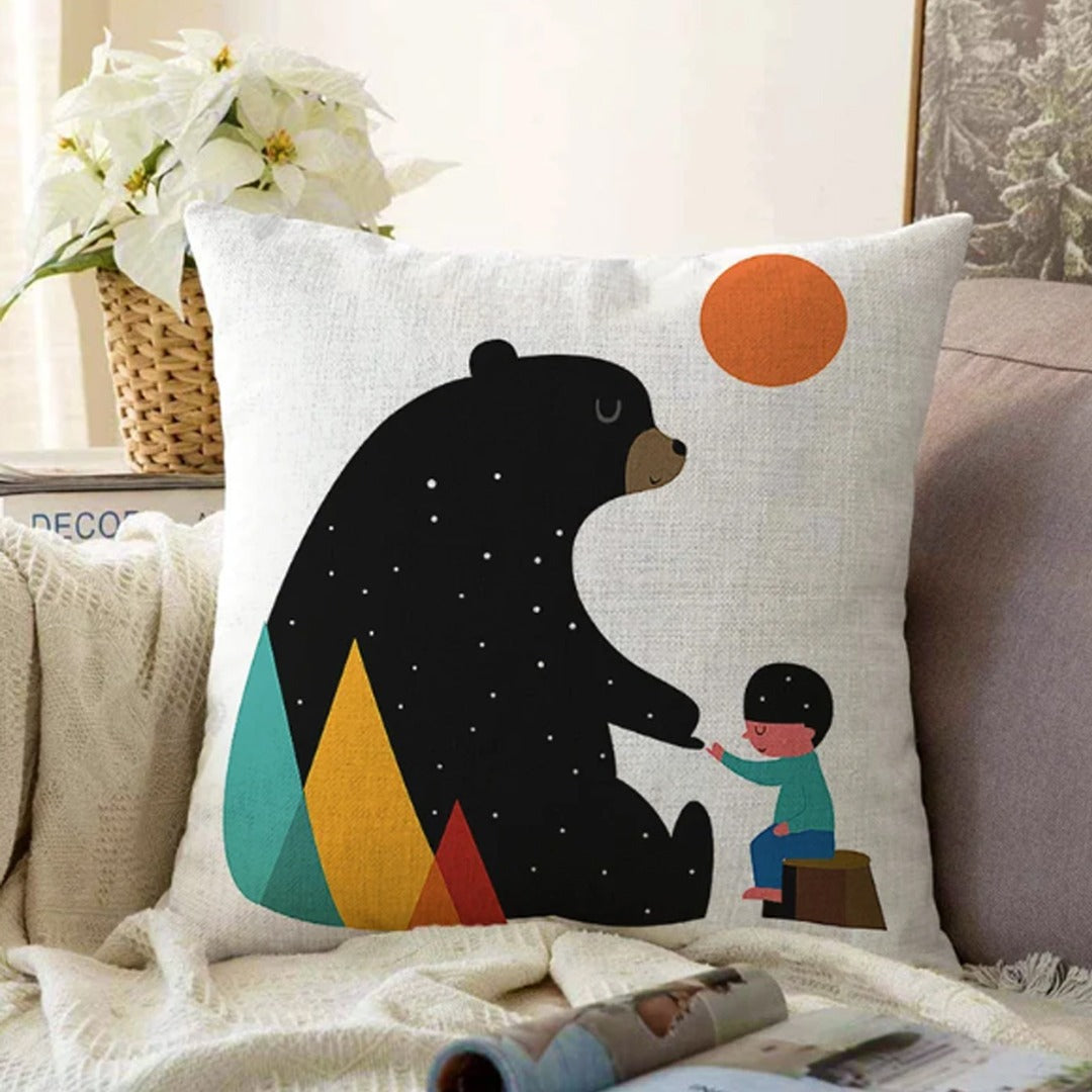 White cushion cover with a black bear, a small child and an orange sun.