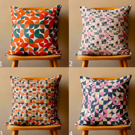 Four colourful geometric cushion covers displayed on wooden chairs.