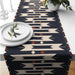 Black table runner with cream stepped motifs and small orange accents.