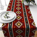 Red table runner with multicoloured geometric diamonds and striped borders.